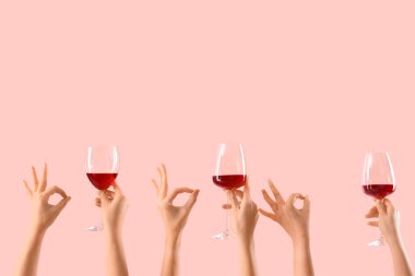 Şarap kadehlerini tutan kadın eller pembe arka planda iyi görünüyor.