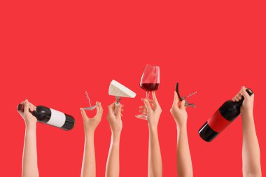 Kırmızı arka planda tirbuşon, peynir, şişe ve şarap bardakları tutan kadın elleri