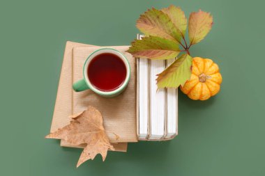 Yeşil arka planda kitap yığınları, balkabağı ve sonbahar yapraklarıyla kompozisyon