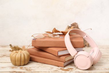 Kitap yığını, kulaklık ve sonbahar yaprakları açık ahşap masa üzerinde.