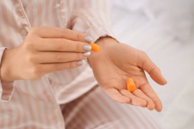 Young woman with ear plugs in bedroom, closeup clipart