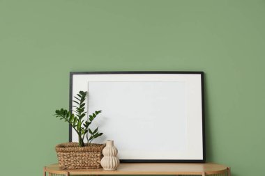 Odadaki yeşil duvarın yanındaki raflarda saksı, vazo ve çerçeve var. Yakın çekim.