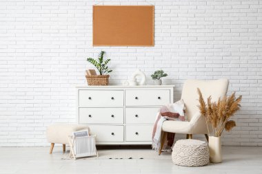 Koltuk, puf, pampas çimen, beyaz duvarın yanındaki çekmecelerin çerçevesi ve göğsü.