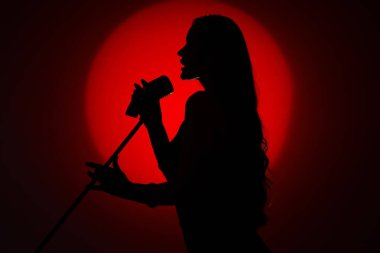 Koyu kırmızı arka planda mikrofonu olan kadın şarkıcının silueti