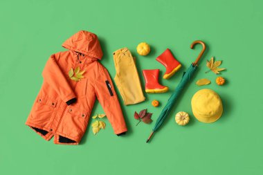 Yeşil arka planda şık çocuk kıyafetleri, aksesuarlar, balkabakları ve sonbahar yaprakları olan kompozisyon