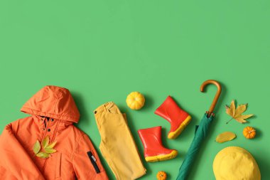 Yeşil arka planda şık çocuk kıyafetleri, aksesuarlar, balkabakları ve sonbahar yaprakları olan kompozisyon