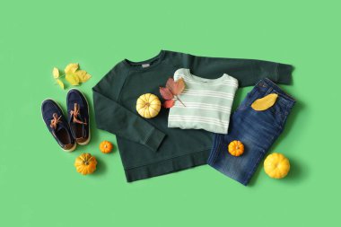 Yeşil arka planda şık çocuk kıyafetleri, ayakkabıları, balkabakları ve düşmüş yaprakları olan kompozisyon