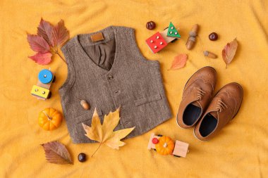 Renkli kumaş arka planında şık çocuk kıyafetleri, ayakkabıları, oyuncakları ve sonbahar dekoru olan kompozisyon