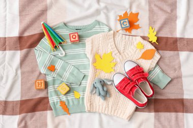 Hafif kumaş arka planında şık çocuk kıyafetleri, ayakkabıları, oyuncakları ve kağıt sonbahar yaprakları olan kompozisyon