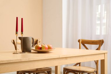 Yemek odasının içinde içinde mumlar, sürahi ve elmalar olan masa.