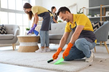 Erkek hademe odada halı süpürüyor.