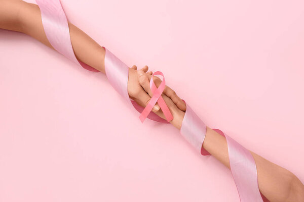 Женские руки и лента осознания на розовом фоне. Концепция рака молочной железы