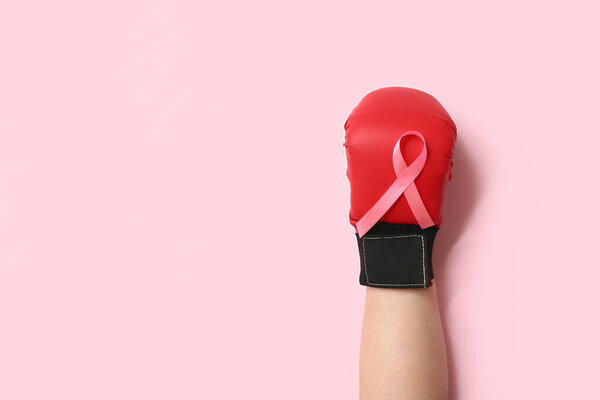 Женская рука в боксерской перчатке с розовой лентой на цветном фоне, крупным планом. Концепция информированности о раке груди