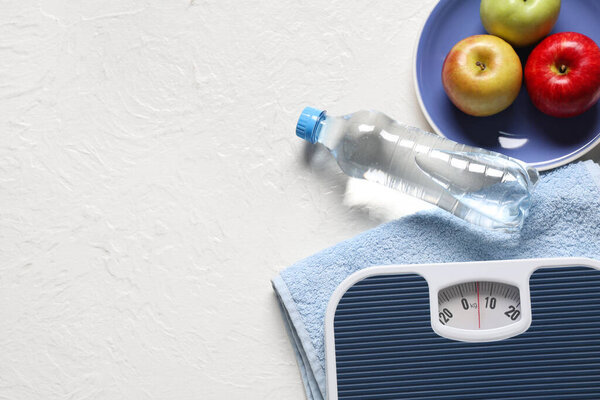 Scales with towel, apples and bottle of water on white grunge background. Weight loss concept