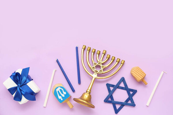 Композиция для празднования Хануки с менорой, дрейделями и подарочной коробкой на сиреневом фоне
