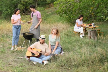 Genç adam barbekü partisinde arkadaşlarıyla gitar çalıyor.