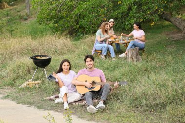 Genç adam barbekü partisinde arkadaşlarıyla gitar çalıyor.