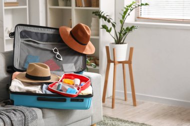 Açık ilk yardım çantası, şık kıyafetler ve yazlık şapkalar odada kanepede.