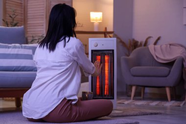 Akşamları elektrikli ısıtıcının yanında elleri ısıtan genç bir kadın.