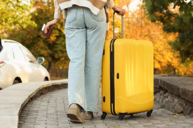 Bavulu ve pasaportu olan bir kadın sonbahar parkında yürüyor.