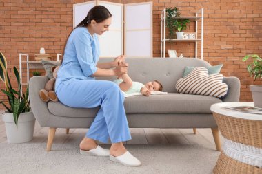 Evdeki kanepede küçük bir bebeği olan kadın bir çocuk doktoru.