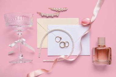 Zarflı alyanslar ve pembe arka planda gelin aksesuarları.