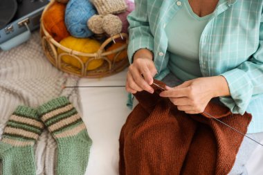 Mature woman knitting sweater with needles in bedroom, closeup clipart