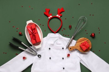 Geyik boynuzları, çatal bıçak, hediyeler ve yeşil arka planda Noel dekoru olan şef üniforması.