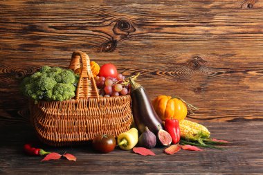 Tahta arka planda farklı taze sebzeler, meyveler ve sonbahar yapraklarıyla dolu bir sepet. Hasat festivali