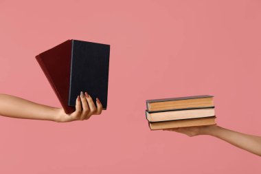 Pembe arka planda bir sürü kitap tutan eller