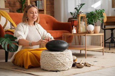 Güzel bir kadın evde halıda glukofon çalıyor.