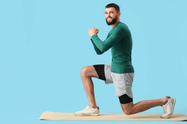 Sportif genç adam mavi arka planda yoga minderi üzerinde egzersiz yapıyor.