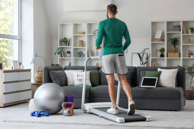 Sportif genç adam evdeki koşu bandında antrenman yapıyor.