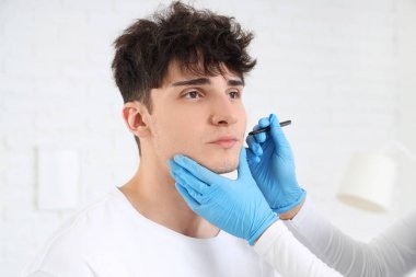 Kadın estetik cerrah klinikte adamın yüzünü işaretliyor.