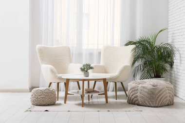 Koltuklar, kahve masası ve puflar oturma odasının içinde.