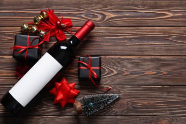 Noel süslemeleri ve tahta arka planda hediye kutuları olan bir şişe şarap.