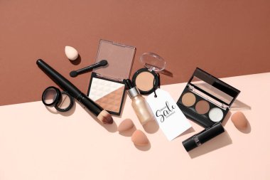 Dekoratif kozmetik ürünleri, makyaj aksesuarları ve renk arkaplanındaki satış etiketleriyle kompozisyon