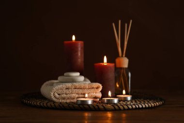 Koyu renk arka plana karşı ahşap masada yanan mumlarla spa kompozisyonu
