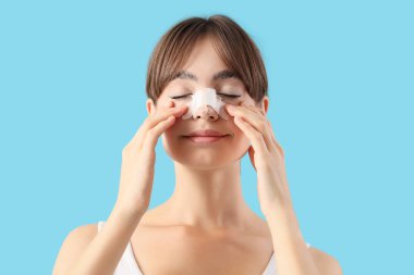 Mavi arka planda sargılı burnu olan güzel, genç bir kadın. Estetik ameliyat konsepti