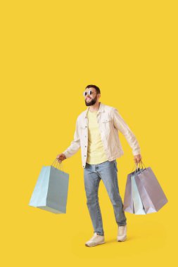 Şık güneş gözlüklü yakışıklı genç adam. Sarı arka planda alışveriş torbaları.