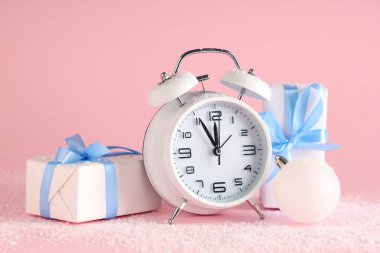 Alarm saati, hediye kutuları ve pembe arka planda Noel balosu.