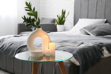 Yatak odasındaki sehpanın üzerinde mumlar ve vazolar yanıyor.