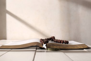 Hafif ahşap masada tespih boncuklarıyla İncil 'i aç