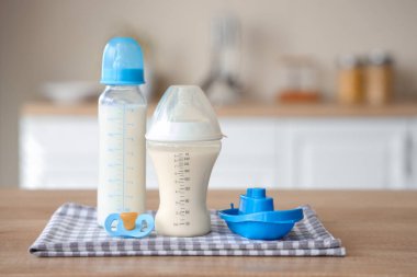 Bebek sütü formülü, emzik ve oyuncak tekne, ahşap mutfak tezgahında.