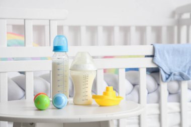 Bebek sütü formülü şişeleri, çıngırak ve oyuncak tekne ışık masasının yanında.