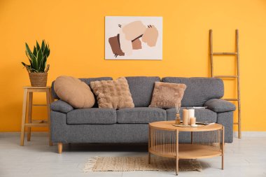 Rahat bir kanepe, çiçek ve renkli duvarın yanındaki masada yanan mumlar.