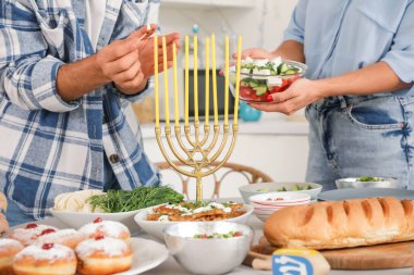 Happy family lighting candles on served dining table in festive kitchen. Hanukkah celebration clipart