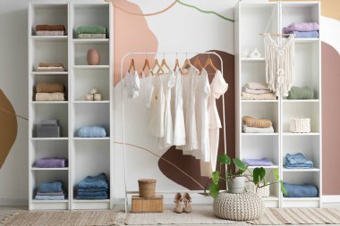 Kadın kıyafetleri ve bitki örtüsüyle aydınlık soyunma odasının şık bir iç mekanı.