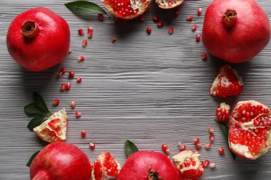 Gri ahşap zemin üzerinde tohum ve yapraklarla taze olgun narlardan yapılmış çerçeve