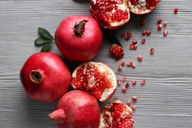 Gri ahşap arka planda tohum ve yapraklarla taze olgun narlar.